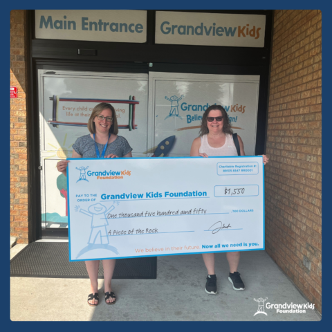 Two women, one from the Grandview Kids Foundation and one from A Piece of the Rock holding a large cheque for one thousand five hundred and fifty dollars for the Grandview Kids Foundation.